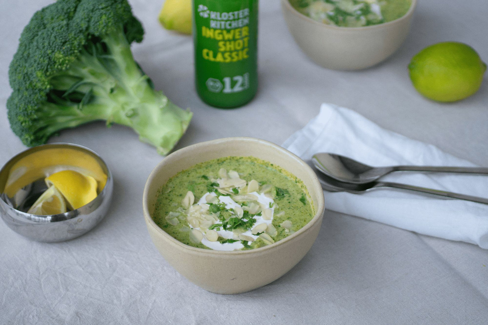 Brokkoli Suppe angerichtet in einer Suppenschüssel. Daneben der Kloster Kitchen Ingwer Shot Classic