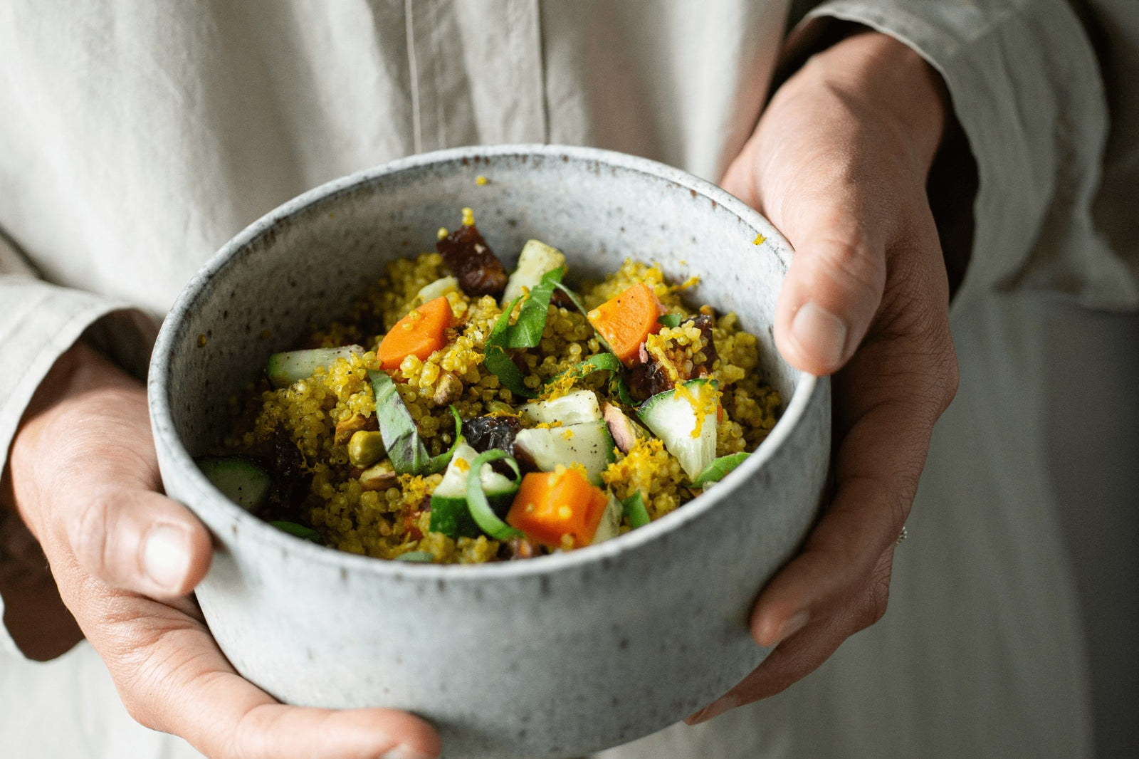 Mani che tengono una ciotola in cui è stata preparata una ciotola di quinoa.