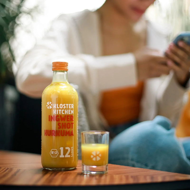 Ginger Shot Turmeric 12SHOTS single bottle stands on a table, next to it poured shot glass