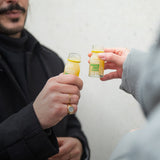 Two people toast with a Ginger Shot Classic 1SHOT in each hand.