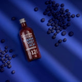 El Vitamin Shot Acai 12SHOTS de Kloster Kitchen, sobre fondo azul. Unos puñados de bayas de acai se esparcen alrededor de la botella de 360 ml. 